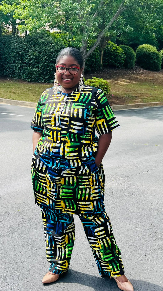 Woman wearing a two-piece Ankara outfit featuring a button-up top and matching baggy pants with an elastic waistband, standing outdoors.