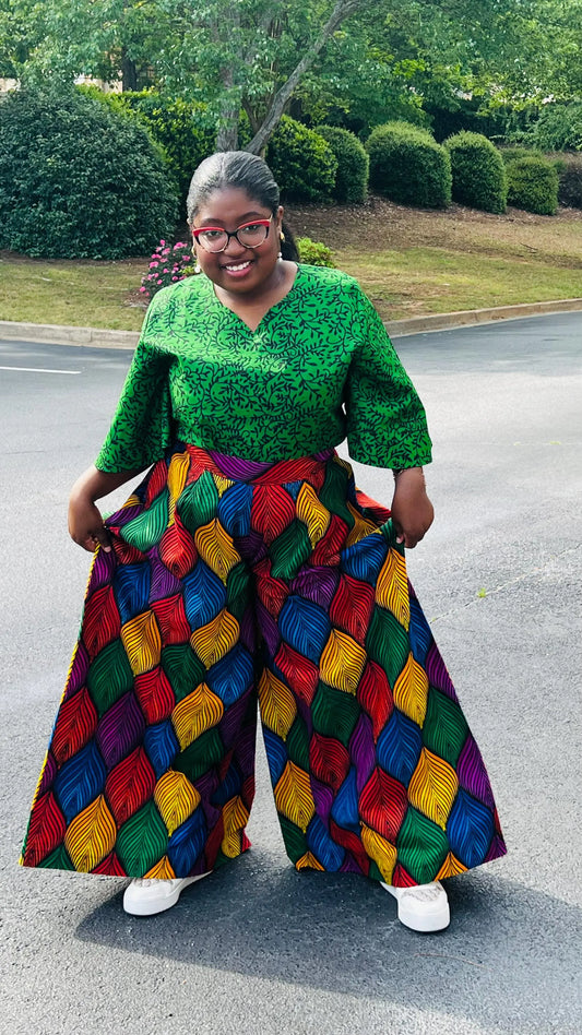 Woman wearing a vibrant two-piece Ankara outfit featuring a flare-sleeve top and matching baggy pants, standing outdoors.